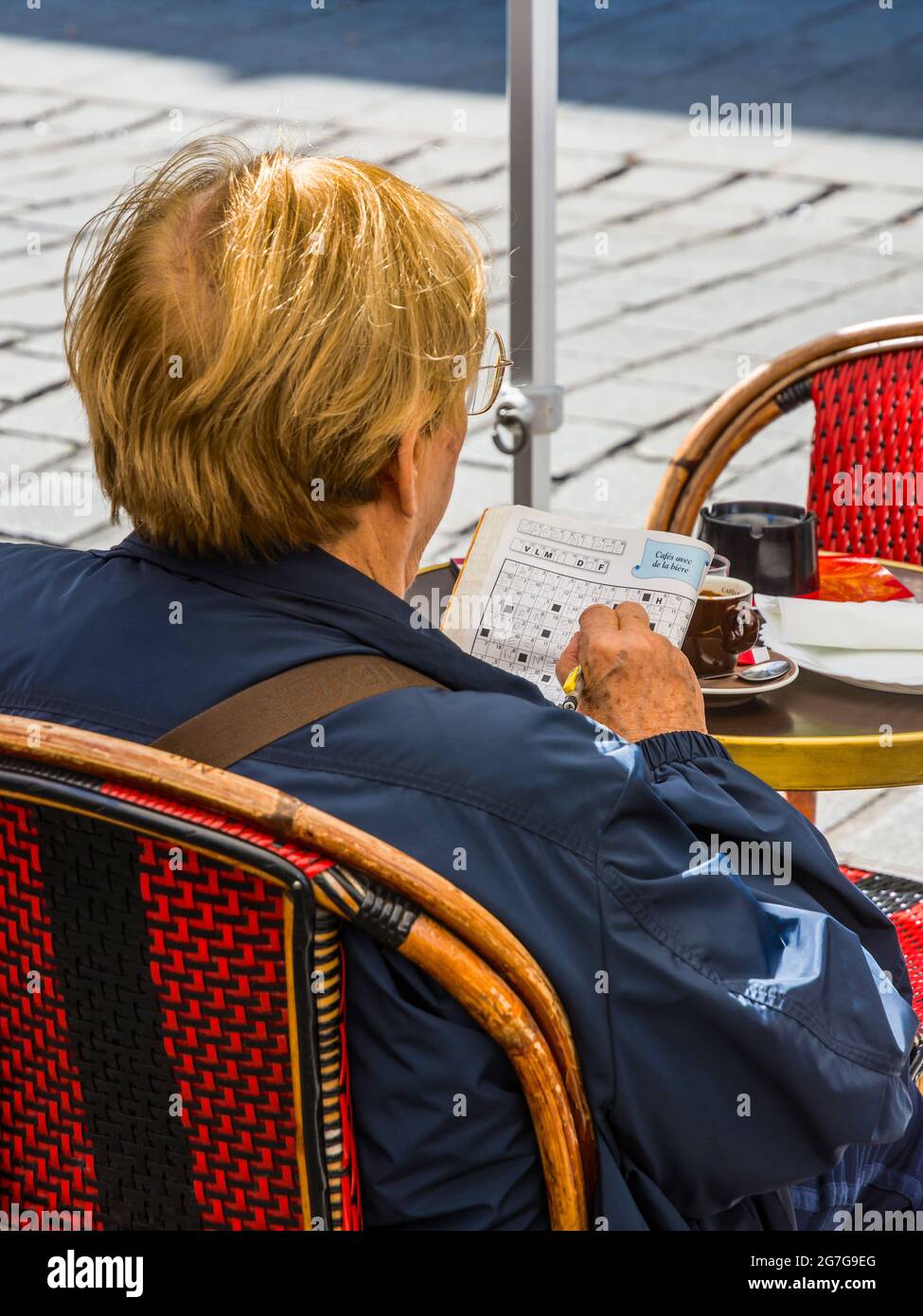 Woman sat at outdoor table doing crossword puzzle - Paris, France. Stock Photo
