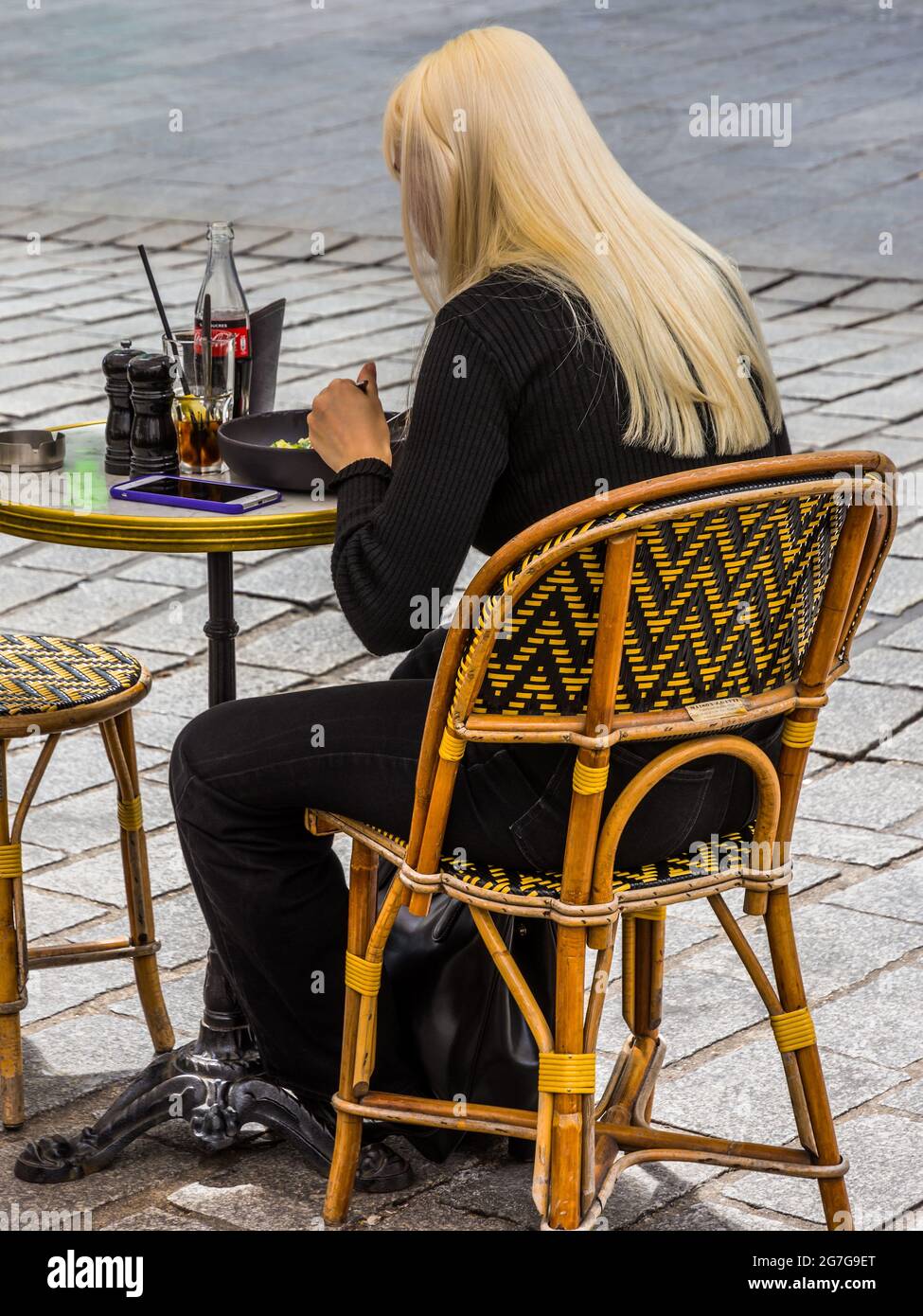Young blonde woman eating lunch at outdoor restaurant table - Paris, France. Stock Photo