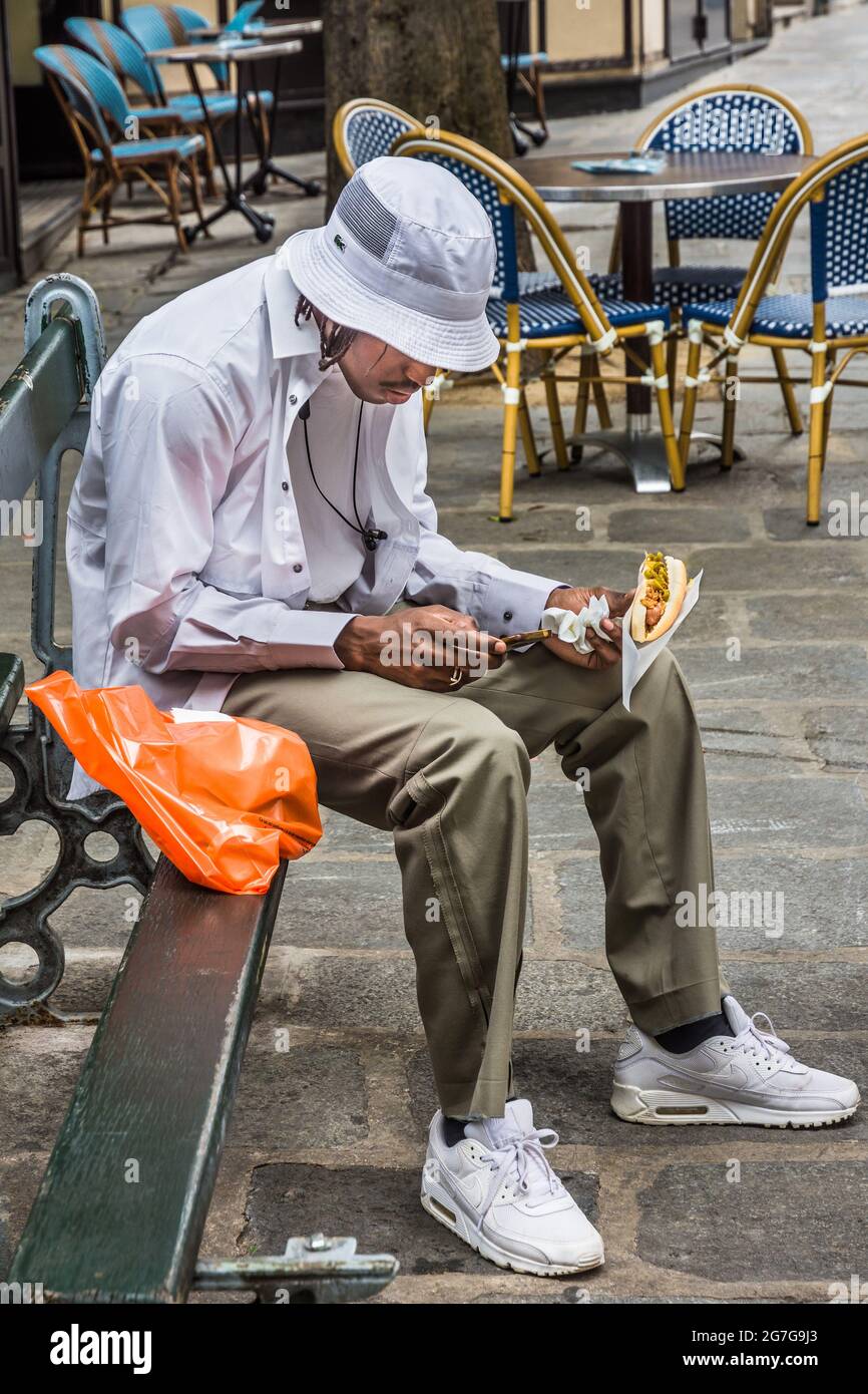 Young black man looking at telephone and holding burger - Paris, France. Stock Photo