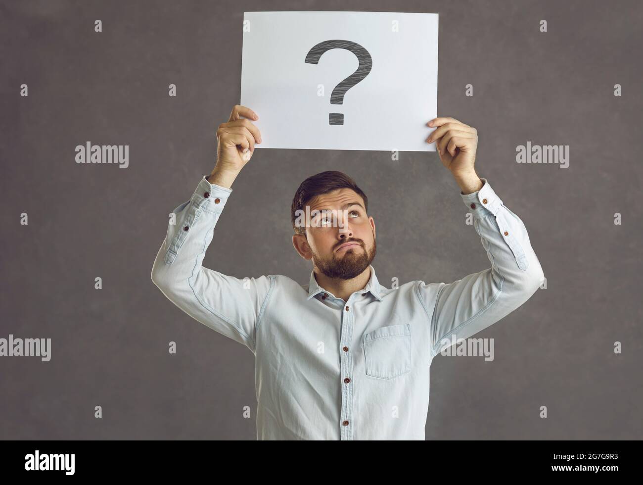 Man holding a sheet of paper with a question mark, thinking and asking himself what decision to take Stock Photo