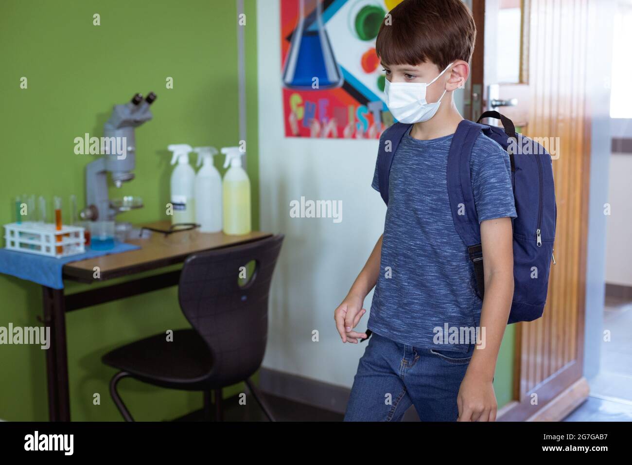 Caucasian schoolboy in classroom wearing face mask and schoolbag Stock Photo