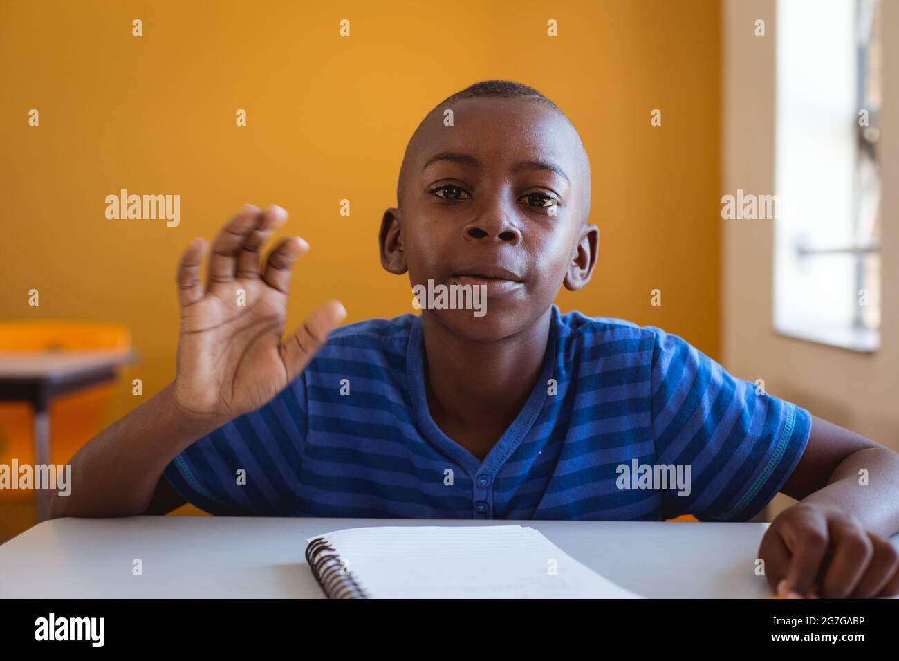 Portrait of african american schoolboy sitting at desk with notebook ...