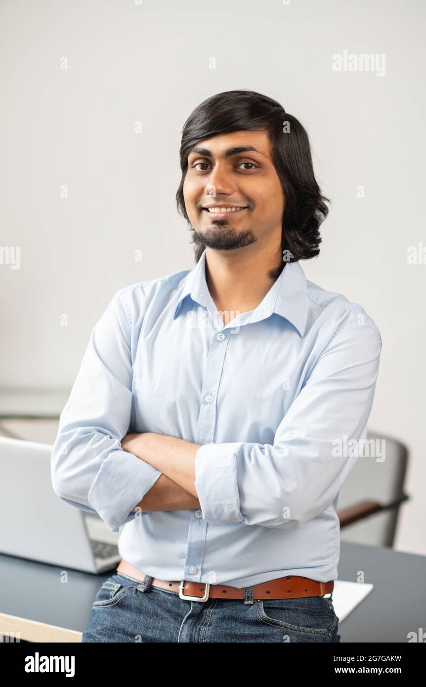 Successful indian businessman stands in the office with arms crossed, vertical portrait of confident middle eastern entrepreneur in smart casual wear looks at the camera and smiles Stock Photo