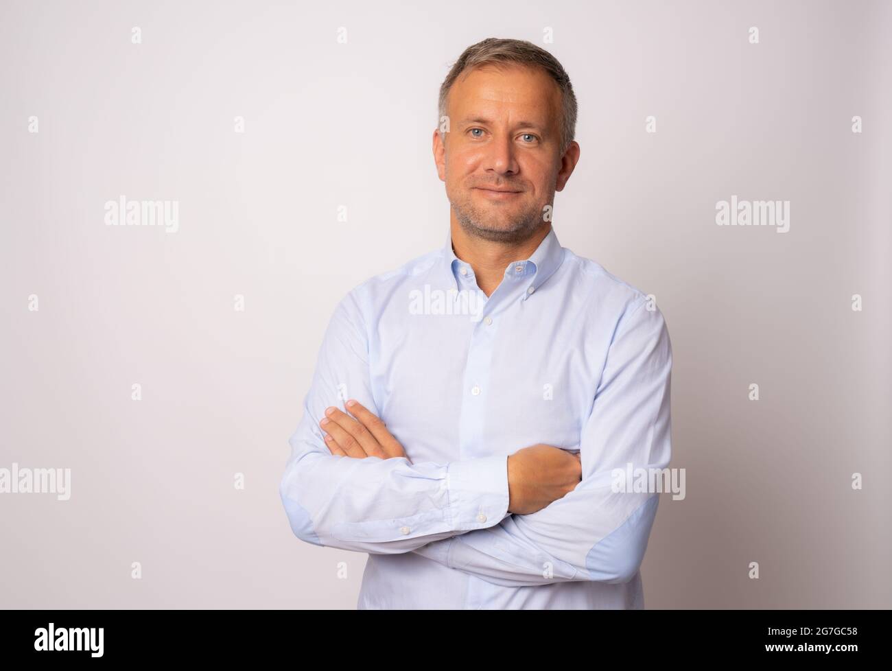 Handsome young man in blue shirt with arms crossed on white background ...