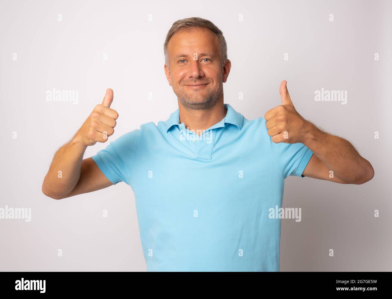 Portrait of cheerful man in basic clothing smiling and showing thumbs ...