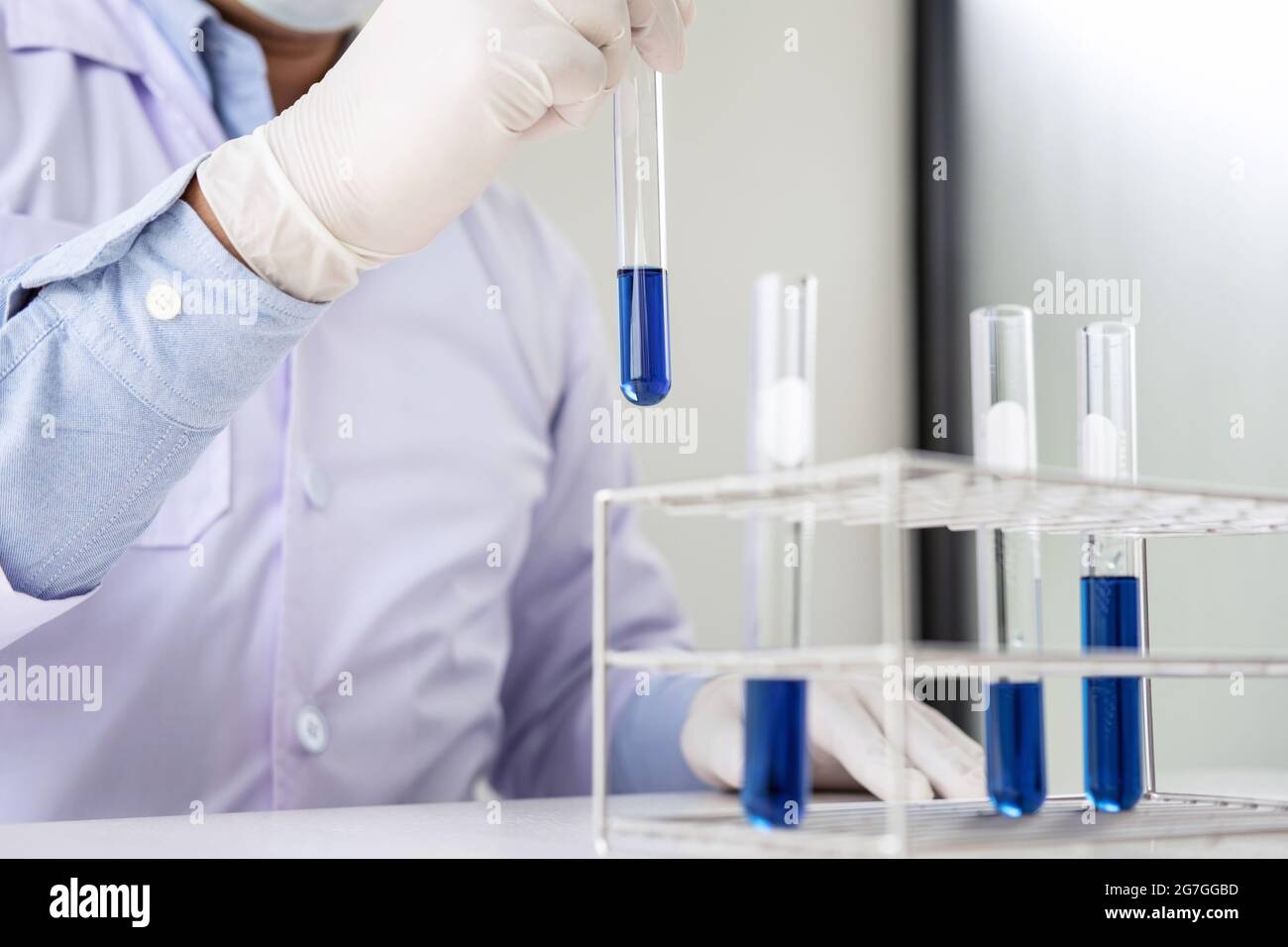 Scientist or medical in lab coat holding test tube with reagent, mixing