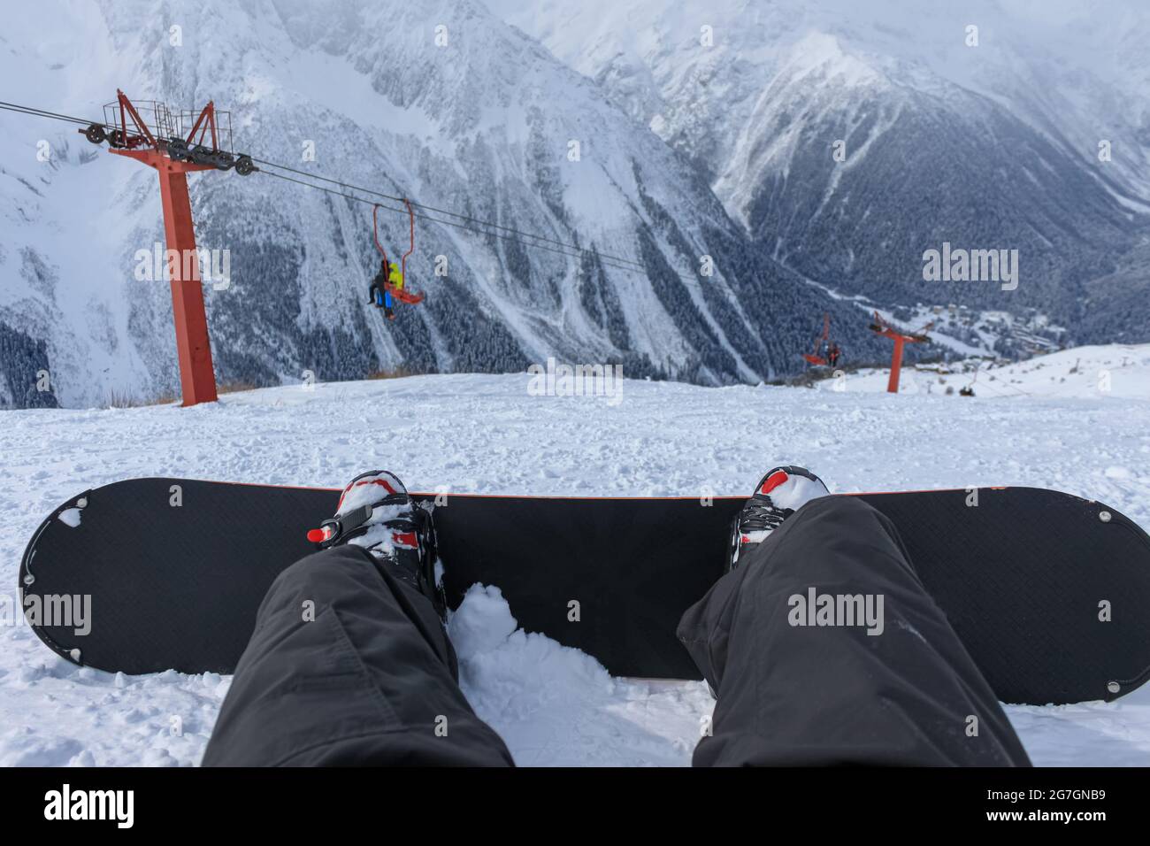 A snowboarder is sitting on the slope of a ski resort and looks at the ...