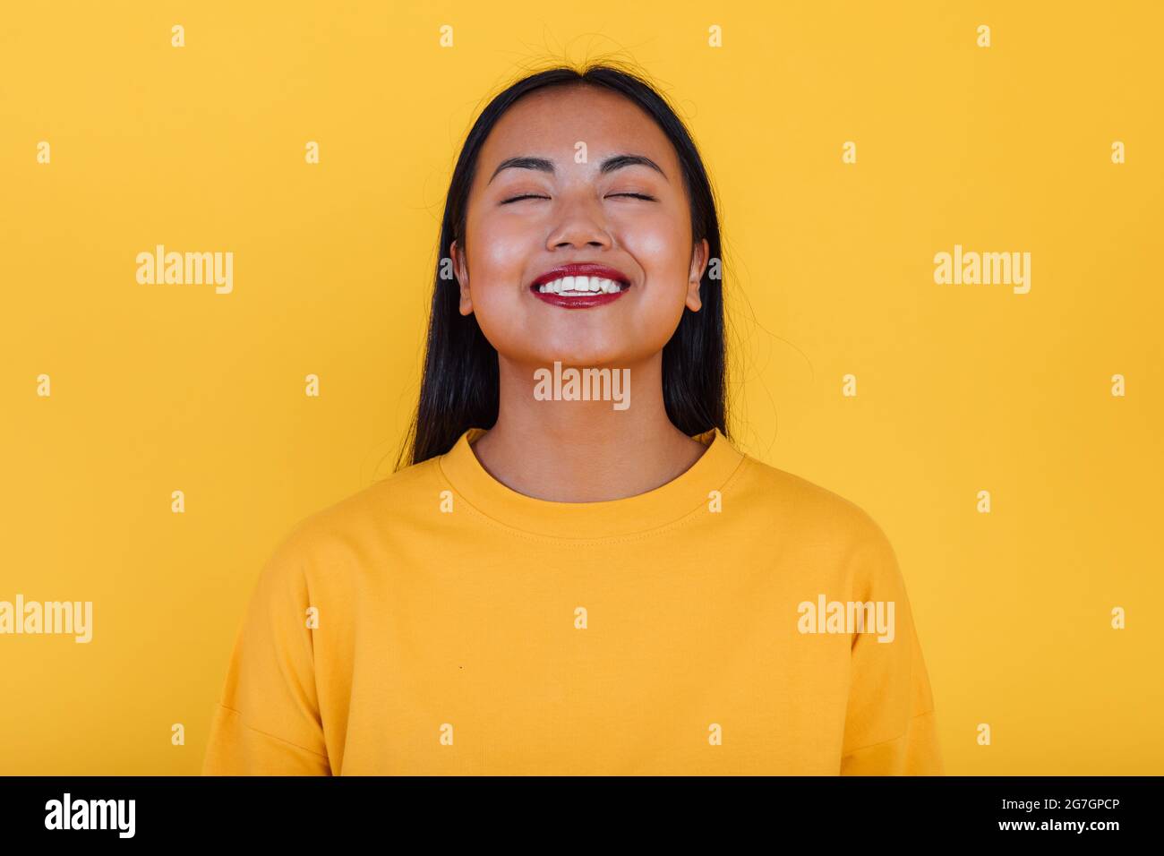 Delighted Asian female standing on yellow background in studio with ...