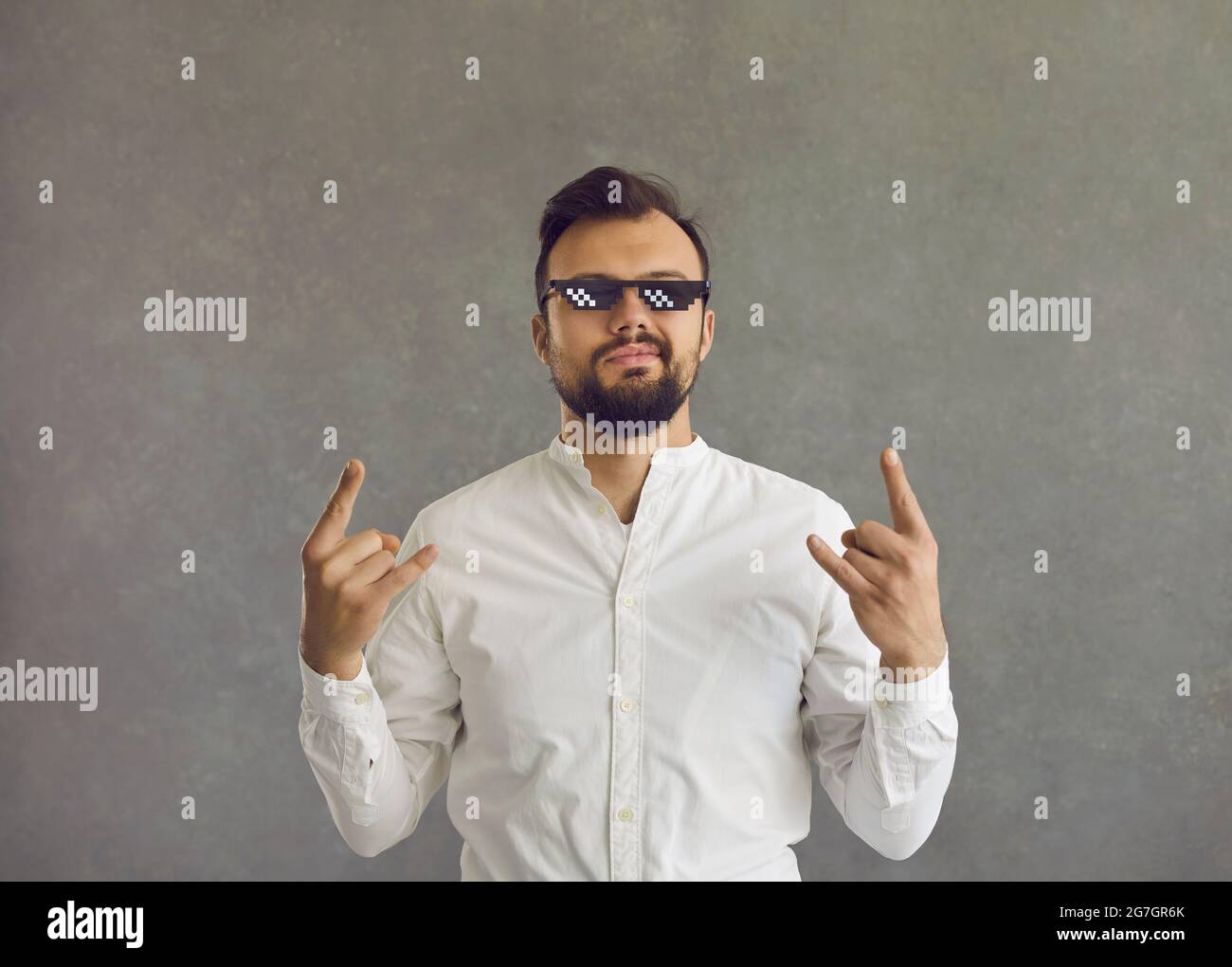 Portrait of young man in thug life glasses smirking and doing rock horn sign gesture Stock Photo