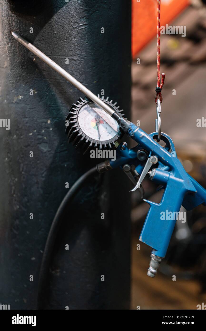 Tyre inflating gun with pressure gauge hanging near wall in shabby bicycle repair workshop Stock Photo