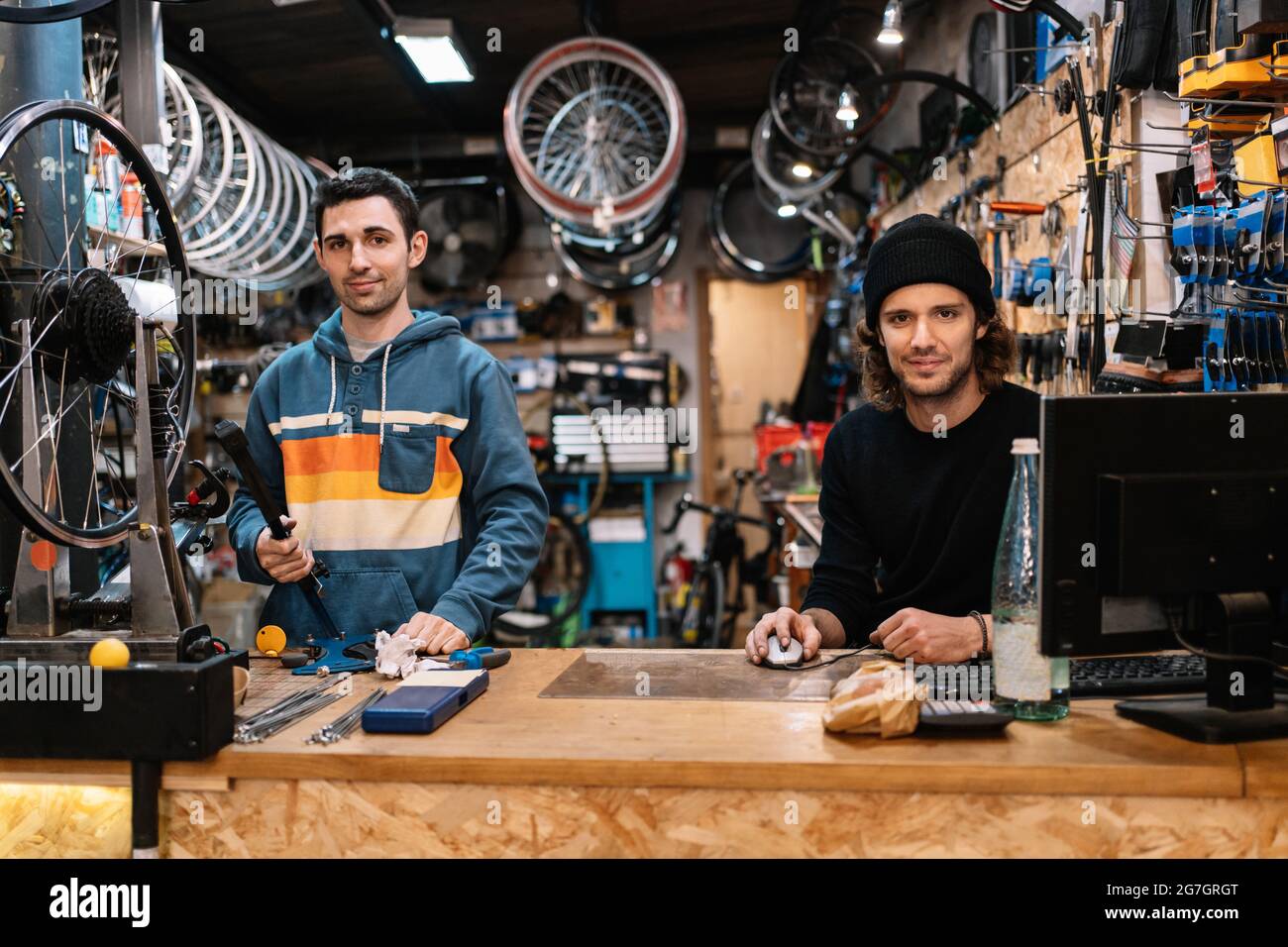 Positive young male technician assembling bike while colleague working on computer in professional workshop Stock Photo