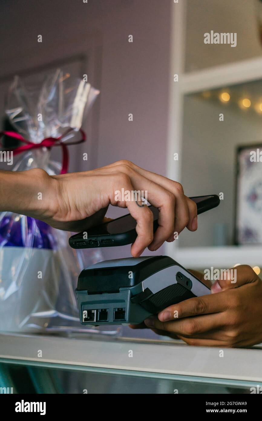 Crop anonymous customer making contactless payment on POS terminal with mobile phone in store Stock Photo