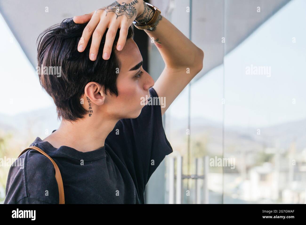 Side view of stylish homosexual man touching hair and looking in glass wall of building in street Stock Photo