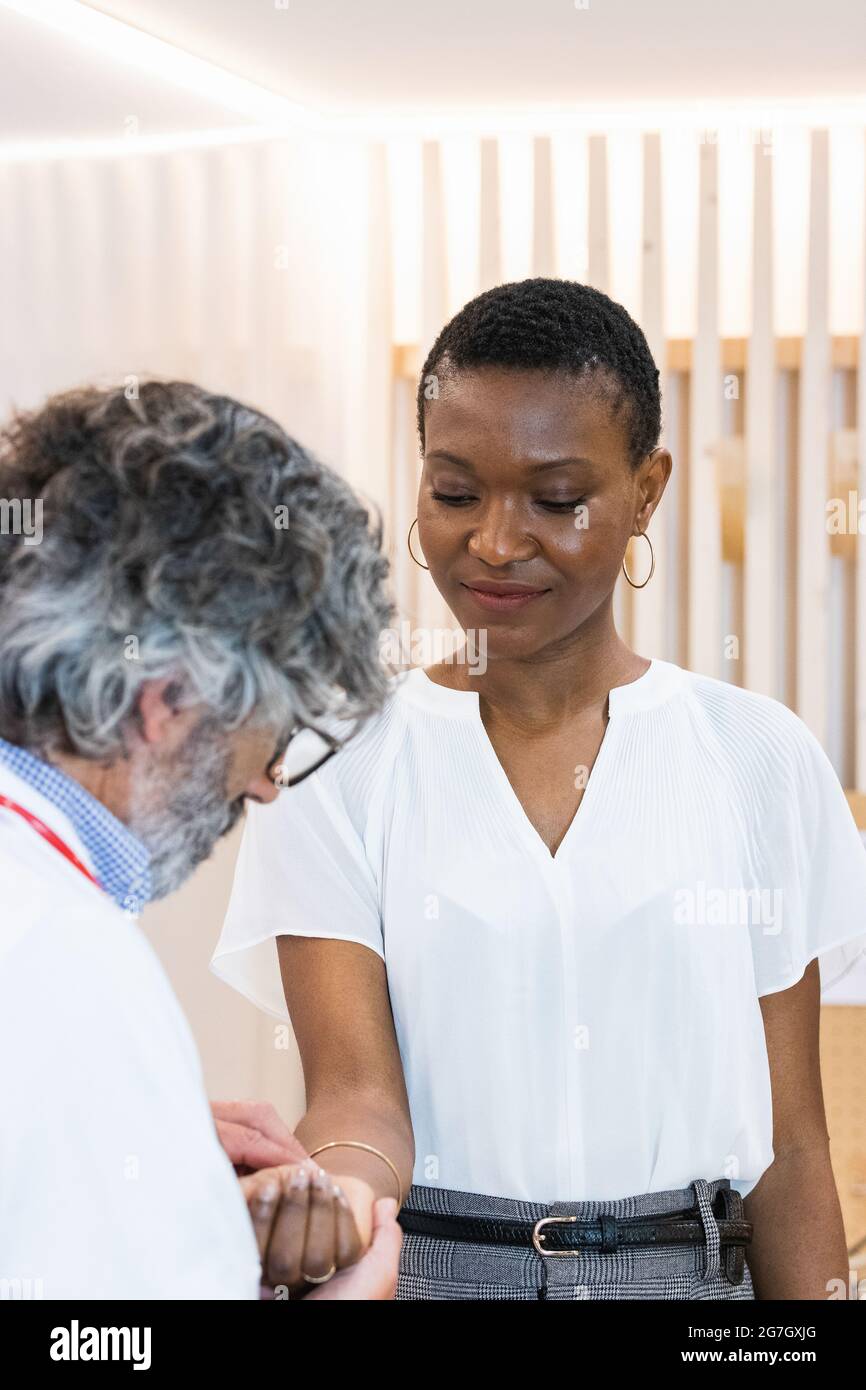 Focused senior male doctor measuring pulse of black female patient