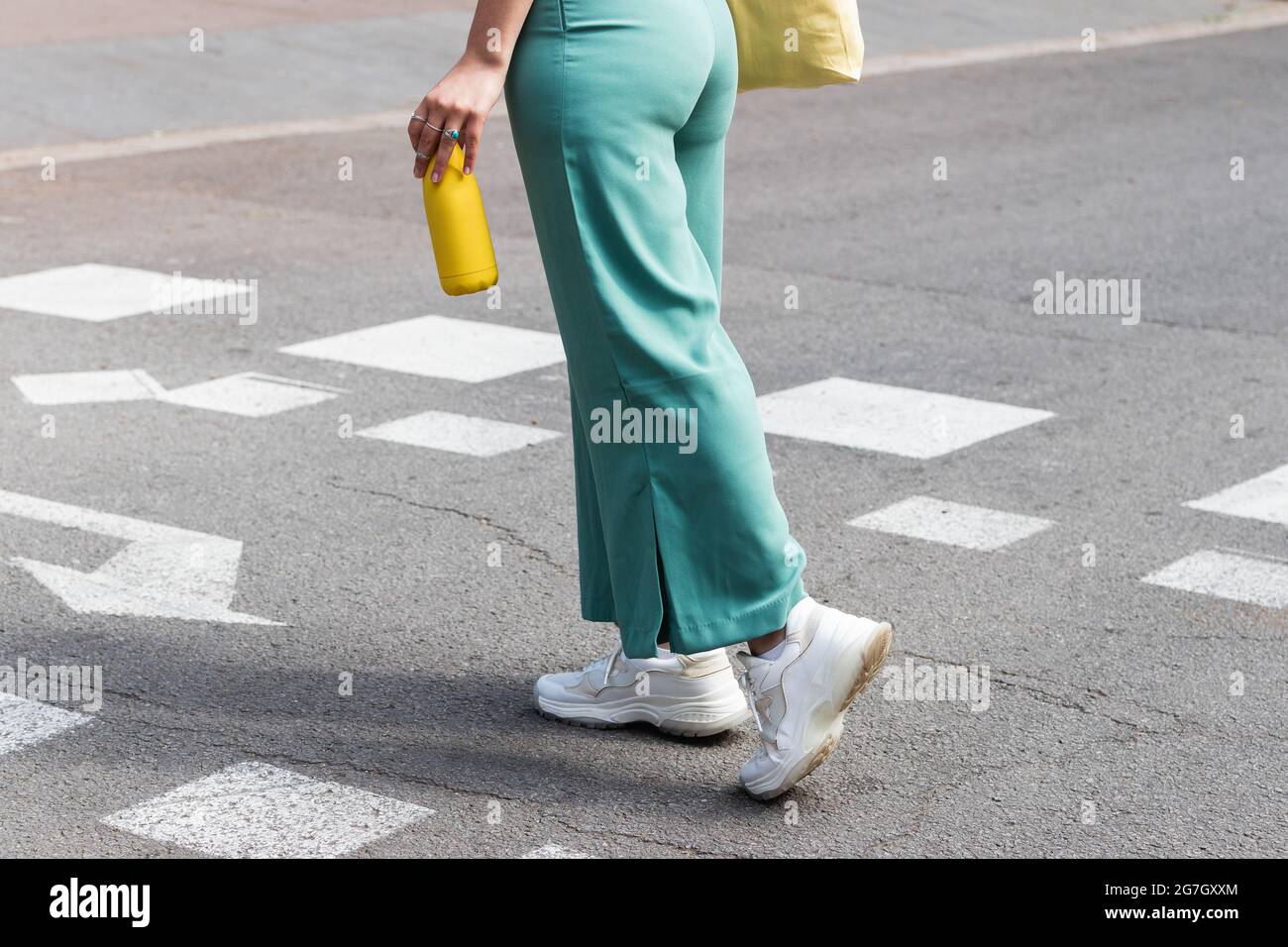 Side view of crop anonymous female with bottle of water walking along crosswalk in city Stock Photo