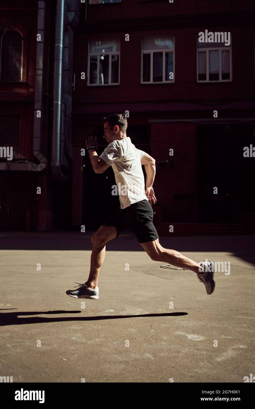 Side view of male running on street while training in city in summer ...
