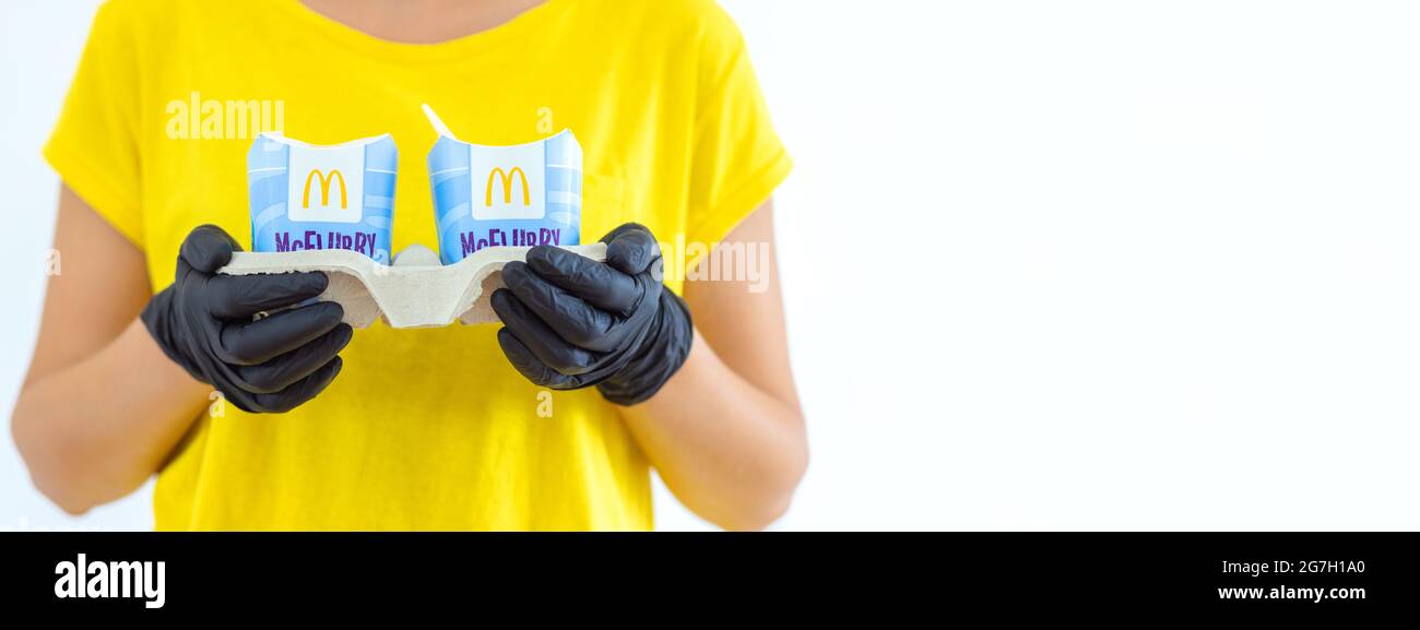 Woman in a yellow t-short holding an ice cream Mcflurry in medical gloves. Delivery McCafe. fast food restaurant Mcdonalds. ake away ice cream Stock Photo