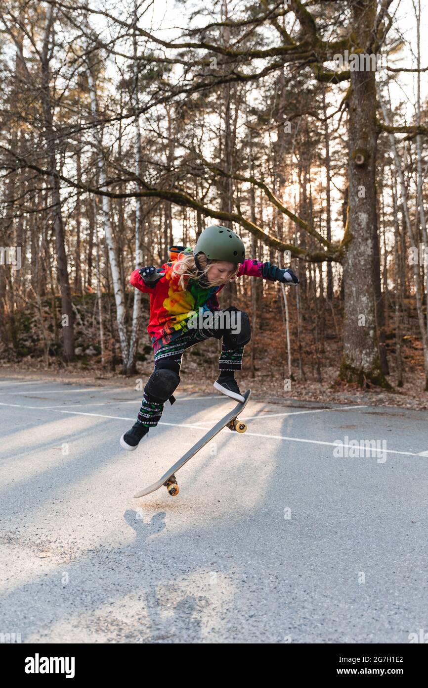 Energetic teenage girl in protective gear jumping above ground with skateboard and performing trick Stock Photo