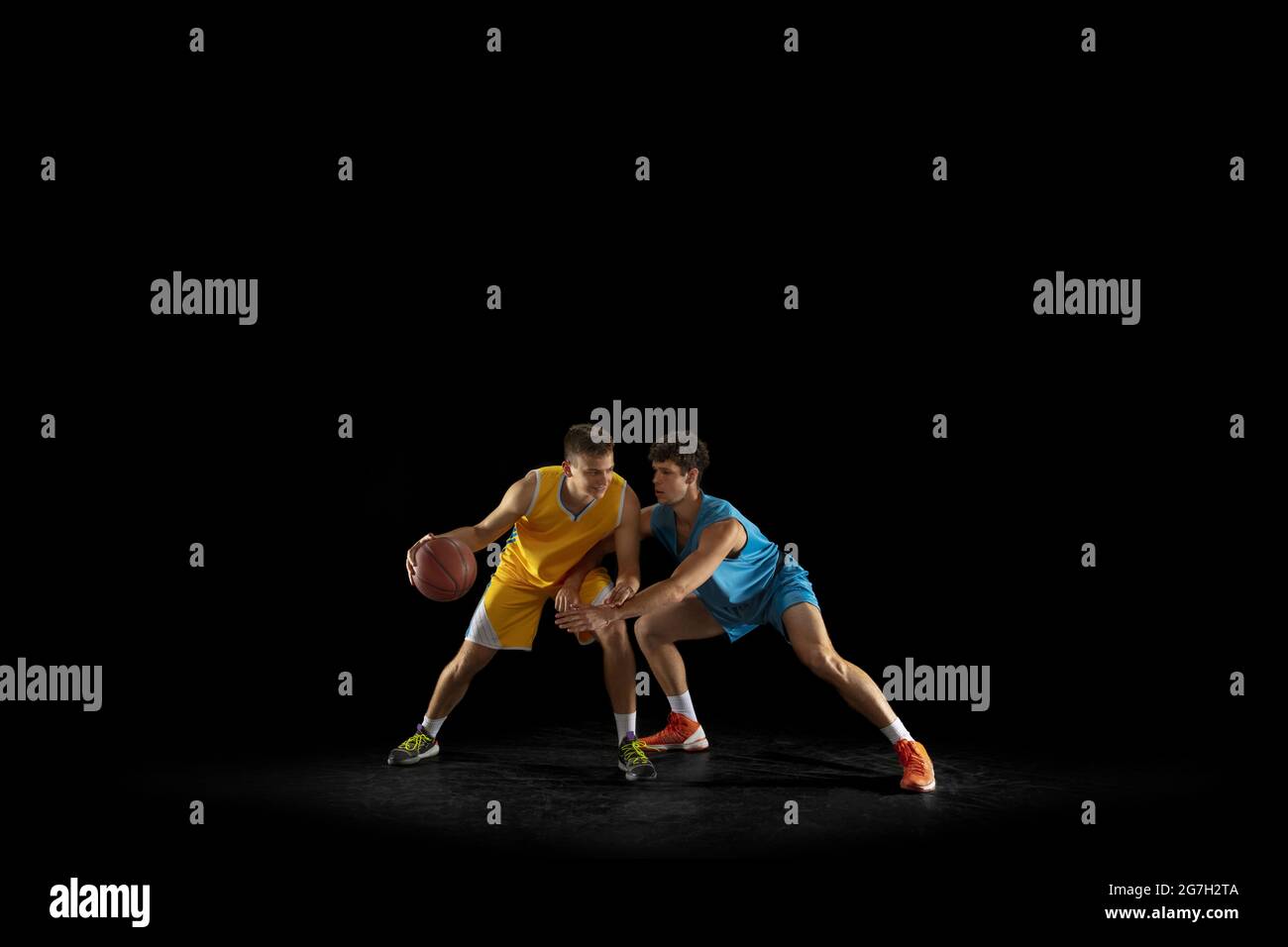 Two basketball players in action and motion isolated on dark black