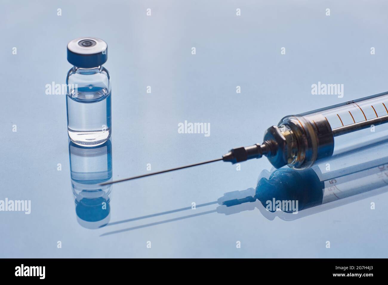 Glass vaccine vial and glass medical syringe on blue glass background ...