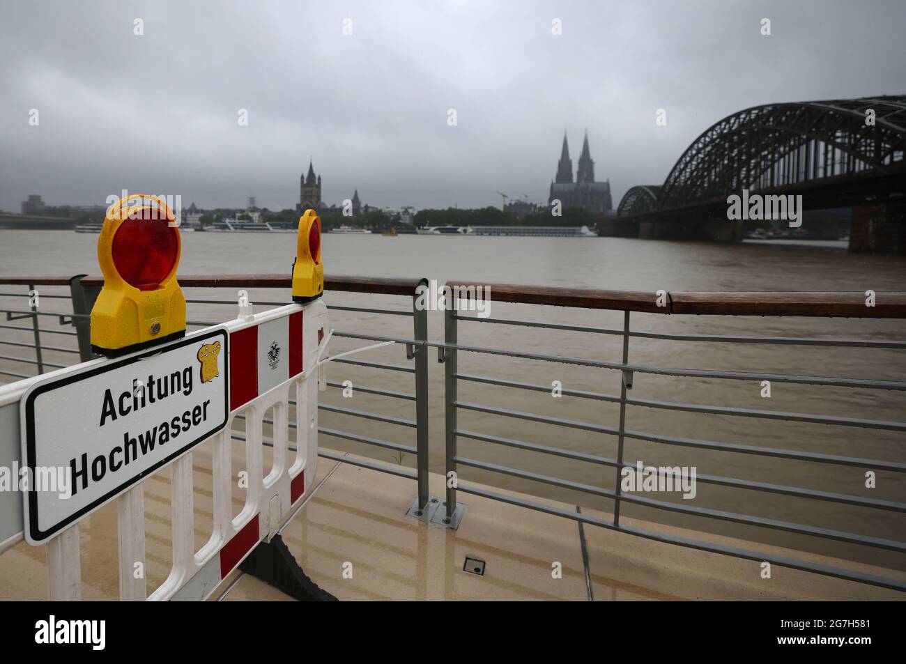 Cologne, Germany. 14th July, 2021. A sign with the inscription 'Attention high water' stands on the banks of the Rhine on a closed path. The heavy rain continues to cause the Rhine to rise. The water level in Cologne on Wednesday morning was 5.47 meters - with a slowly rising trend. Credit: Oliver Berg/dpa/Alamy Live News Stock Photo