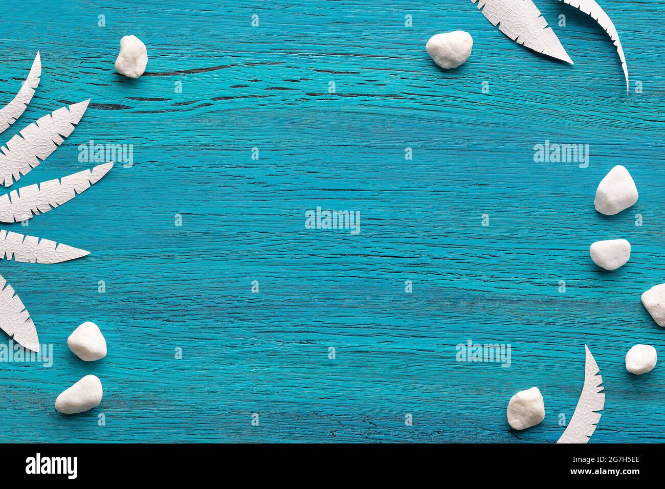 Abstract grungy blue wooden background with exotic paper leaves made of paper and white stones. Copy-space, place for text. Flat lay, top view. Stock Photo