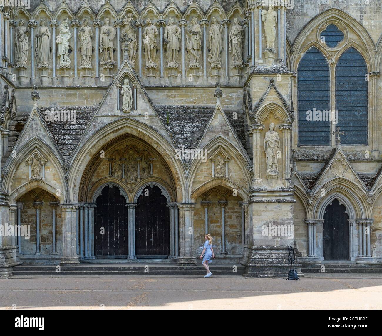 Salisbury, Wiltshire, UK, 14th July 2021, Weather: A warm summer’s day in the grounds of Salisbury Cathedral with temperatures up into the mid 20s and rising as a heatwave builds from the south. A young woman poses for selfies under the gaze of the north facade. Credit: Paul Biggins/Alamy Live News Stock Photo