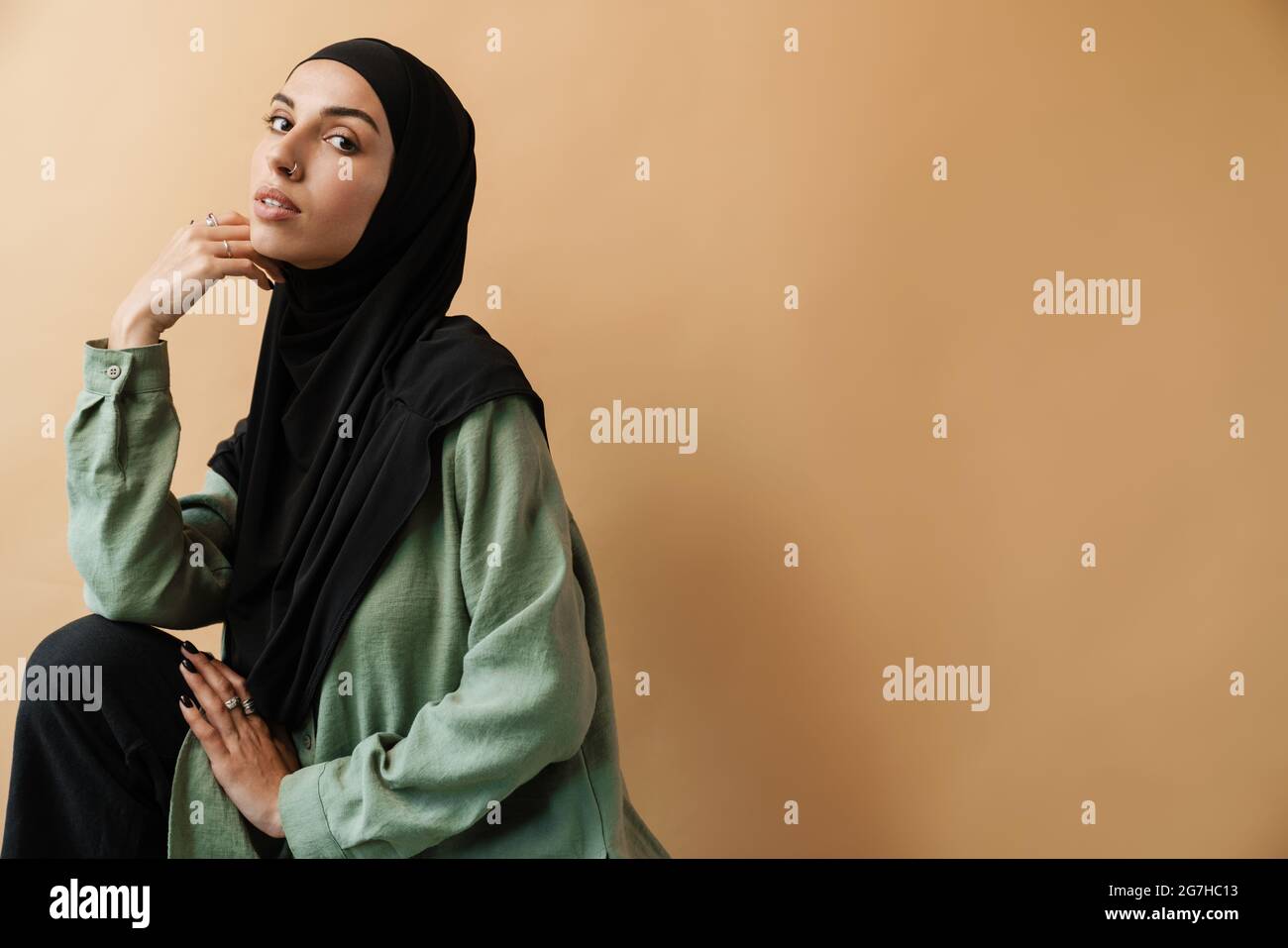 A muslim woman in hijab posing and looking at the camera while standing ...