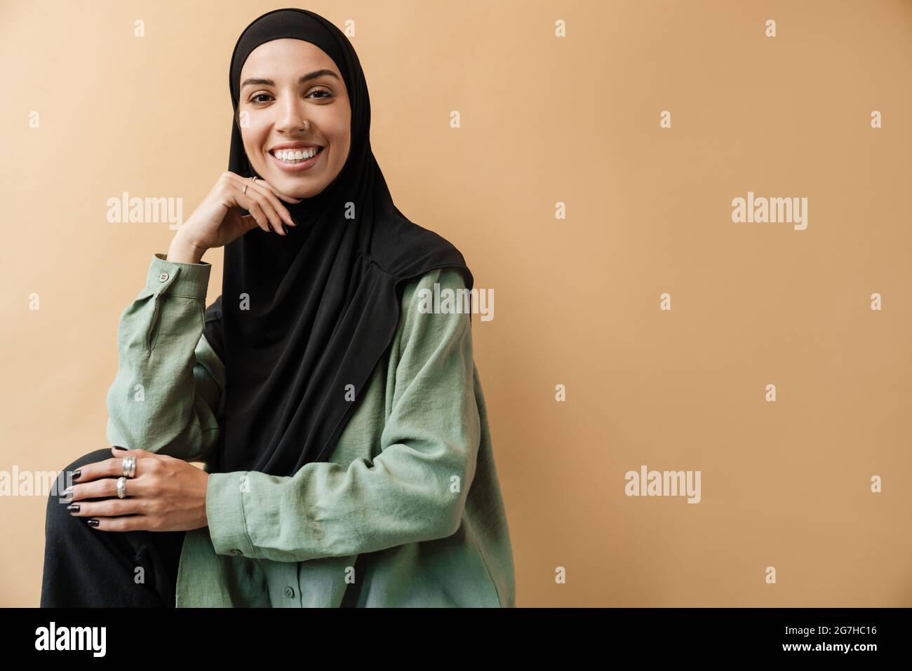 A smiling muslim woman in hijab posing and looking at the camera while ...
