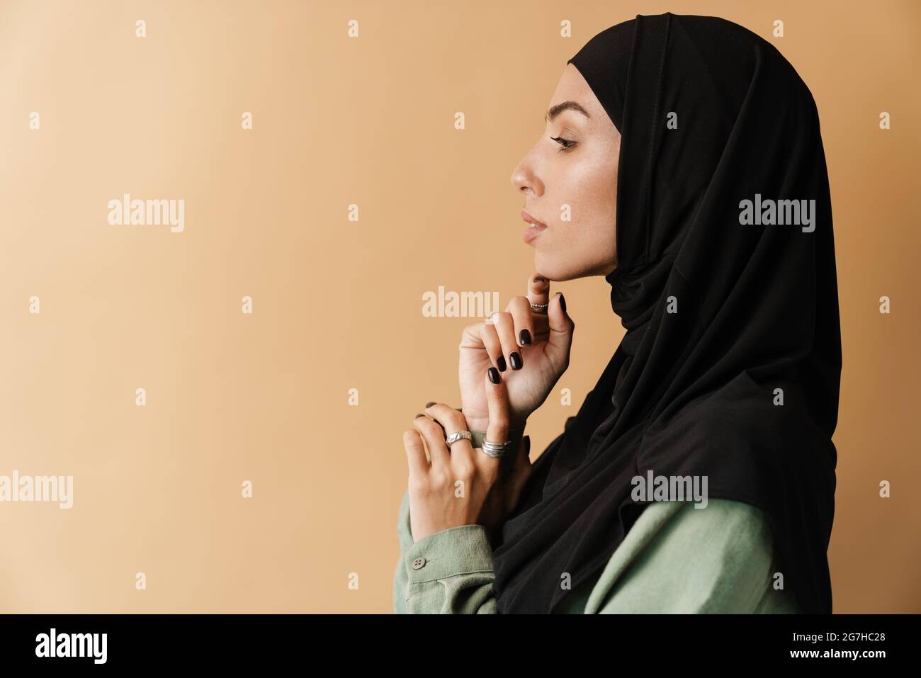 Portrait of a young muslim woman in hijab standing over beige ...
