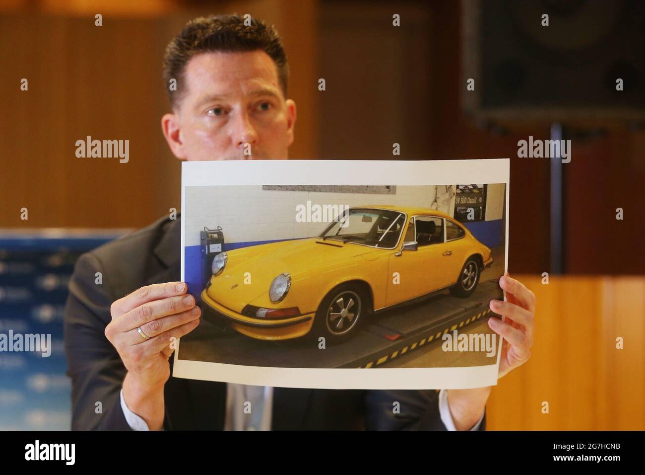 Duesseldorf, Germany. 14th July, 2021. Investigator Raimund Dockter shows a photo of one of the stolen yellow Porsches. Police presented the results of an international raid against classic car thieves. The gang allegedly stole old Mercedes and Porsche cars as well as motorcycles worth almost four million euros. Credit: David Young/dpa/Alamy Live News Stock Photo
