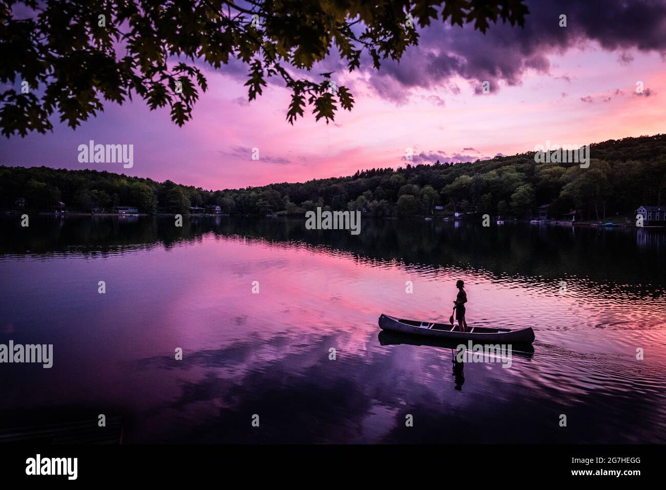 Canoeist stands up in open canoe while paddling on a small lake near Cooperstown, NY, at sunset. Stock Photo