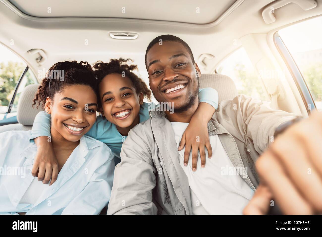 Joyful African American Family Hugging Sitting In Car During Summer Road Trip. Parents And Daughter Posing In New Auto Smiling To Camera. Transportati Stock Photo