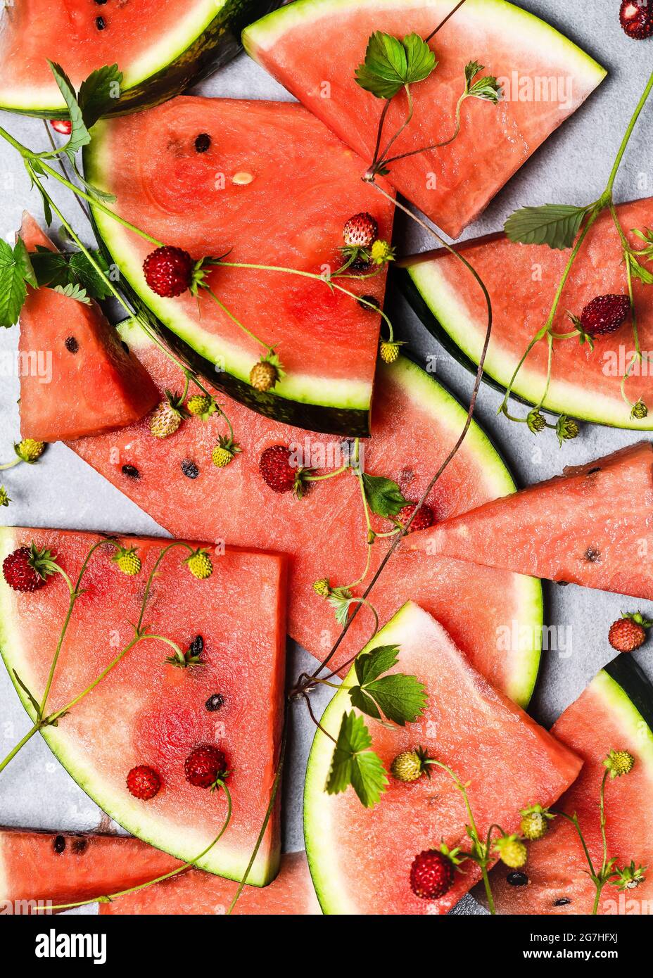 Pile of sliced fresh watermelons and wild strawberries with green leaves. Healthy food concept. Top view. Stock Photo