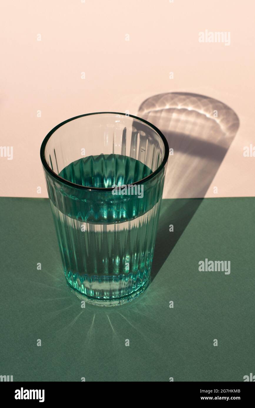 Green water glass with harsh shadow on colored background. Close up. Stock Photo