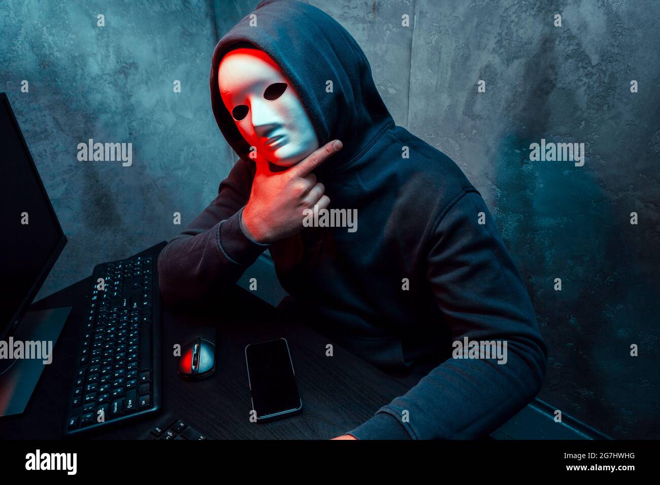 Anonymous hacker wearing face mask working on computer in dark room Stock Photo