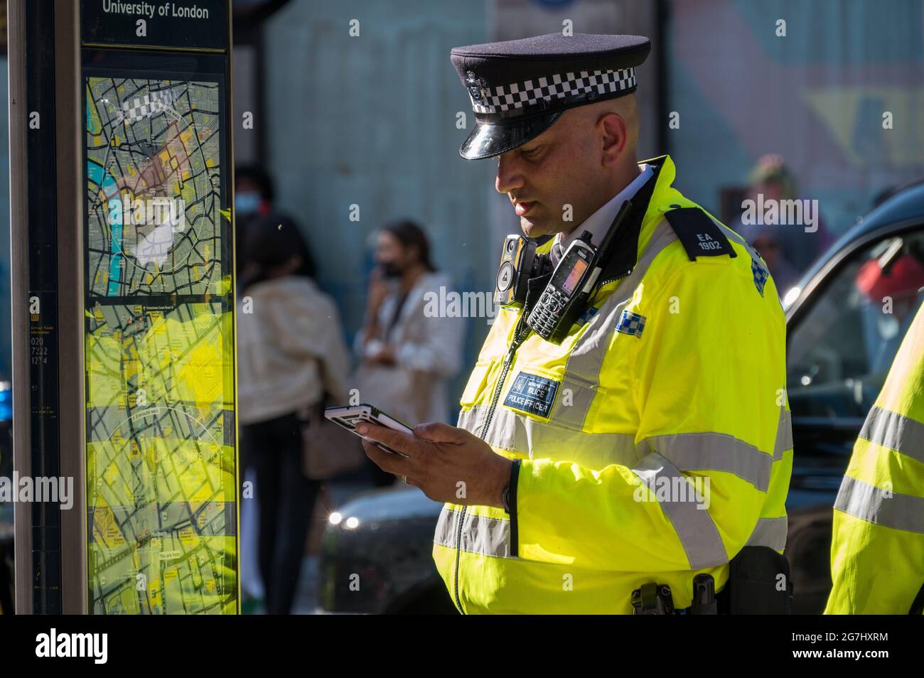 LONDON - MAY 29, 2021: British police officer in a high visibility jacket looks at a mobile cell phone Stock Photo