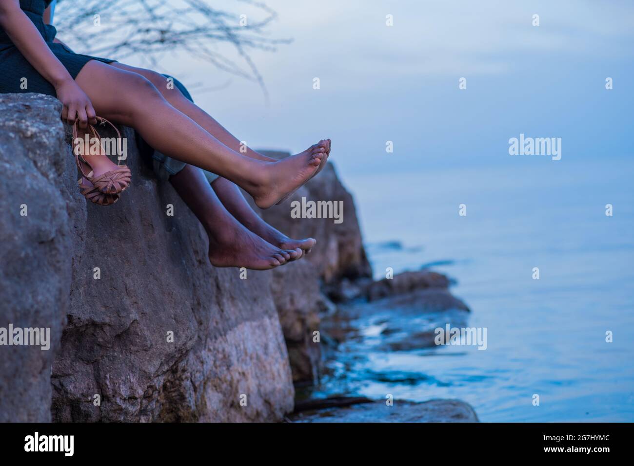 Affectionate African couple sitting on the edge of a cliff by the lake or ocean in late evening during the blue hour at twilight. Stock Photo