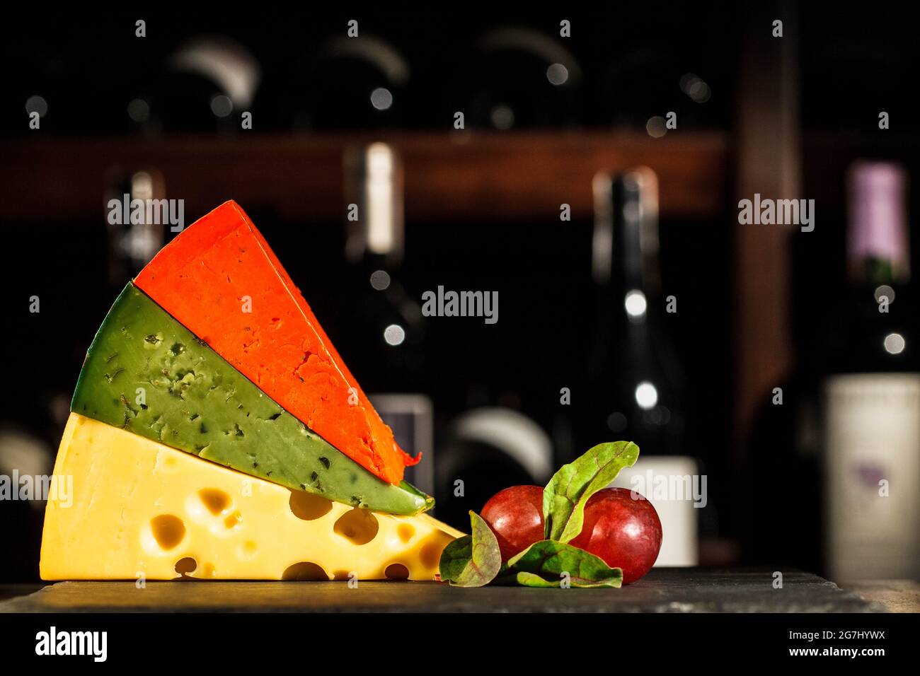Pieces of orange, green and Swiss cheese lie on each other on plate with grape Stock Photo