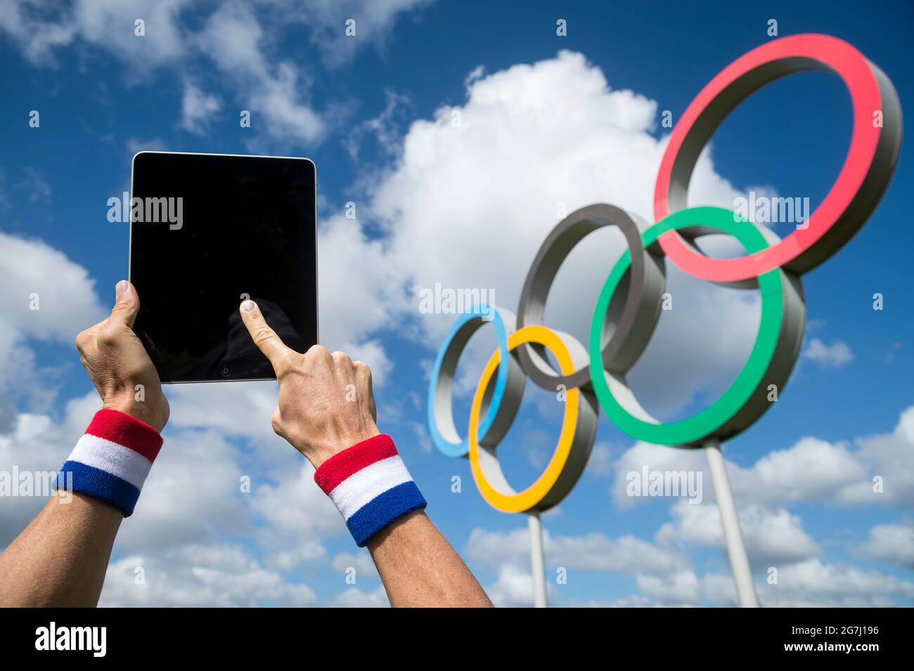RIO DE JANEIRO - APRIL, 2016: Athlete wearing a red, white and blue wristband touching the screen of a tablet computer in front of Olympic Rings Stock Photo