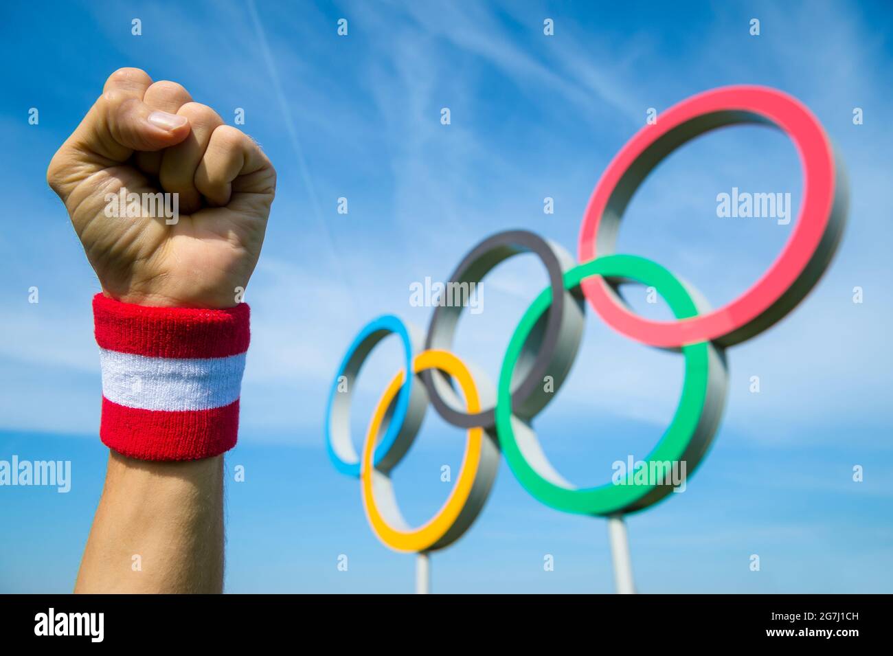 RIO DE JANEIRO - CIRCA MAY, 2016: Japanese athlete wearing red and white wristband punches the air with his fist in front of Olympic Rings Stock Photo