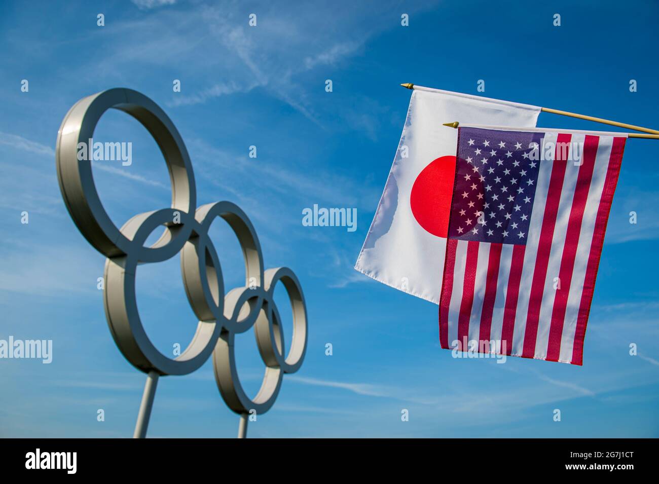 RIO DE JANEIRO - MARCH, 2016: Flags of USA and Japan hang together in front of a large set of shiny metallic Olympic Rings under bright blue sky. Stock Photo