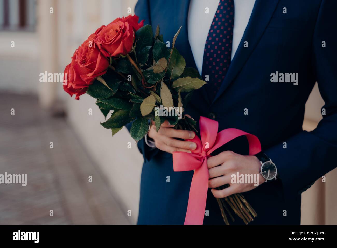 Man dressed in blue suit holding bouquet of red roses Stock Photo