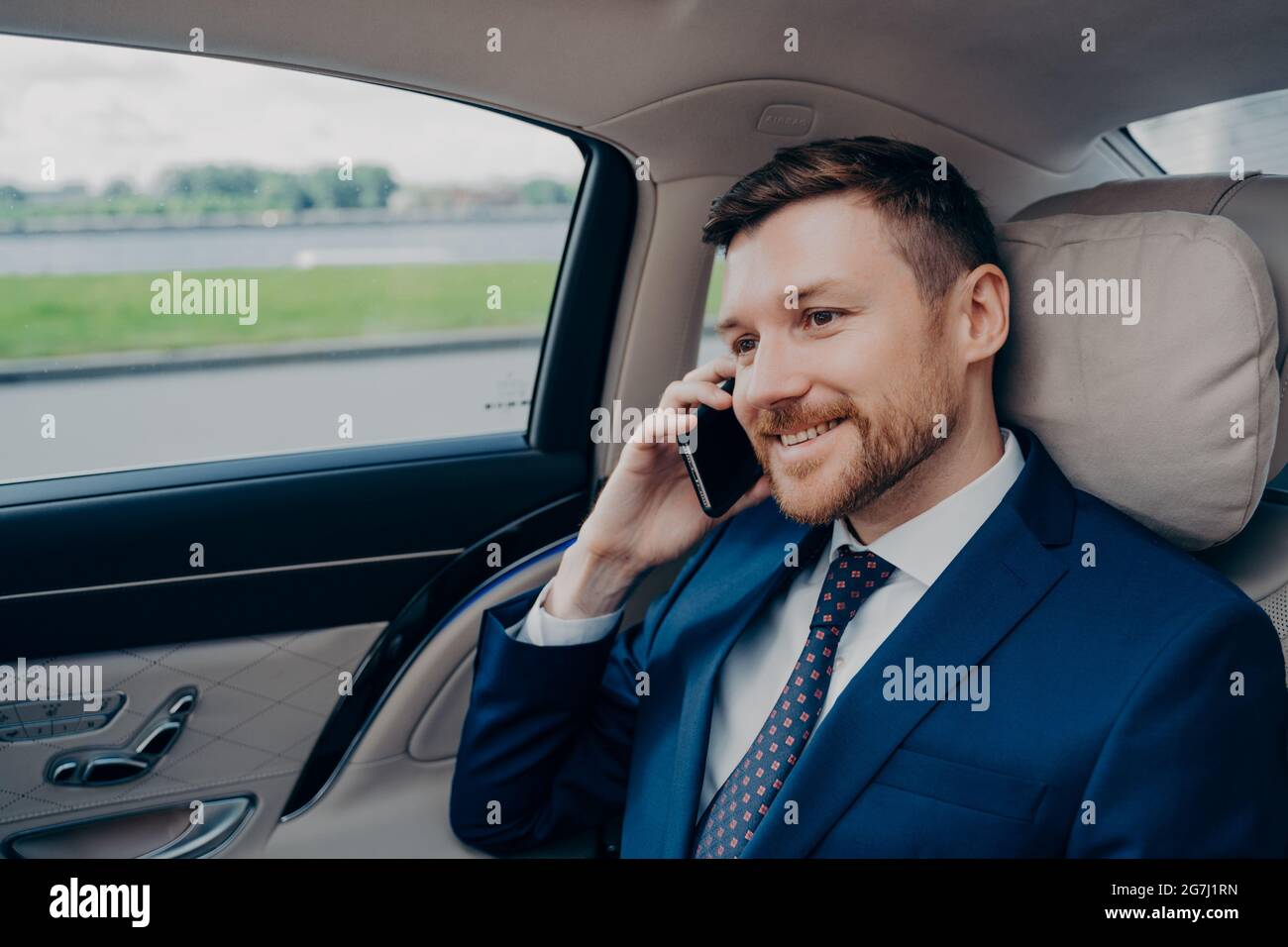 Attractive skilled banker in formal suit riding in corporate car and talking on cellphone Stock Photo