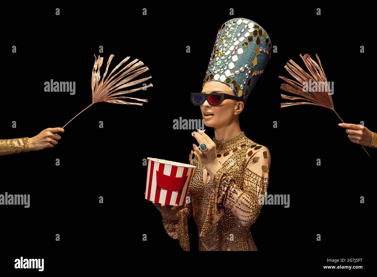 One young woman in image of Nefertiti in art performance watching movie isolated on dark background. Retro style, comparison of eras, humor concept. Stock Photo