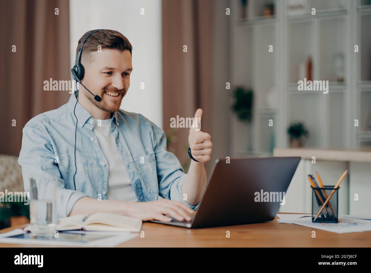 I like it. Glad bearded adult man has video conference keeps thumb up likes something focused at laptop computer has distance job interview dressed Stock Photo