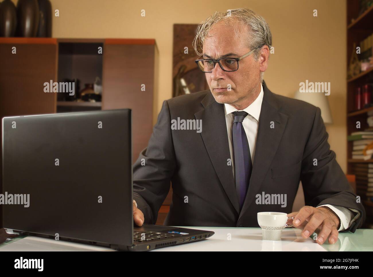 businessman having coffee and teleworking from home with laptop due to covid restrictions Stock Photo