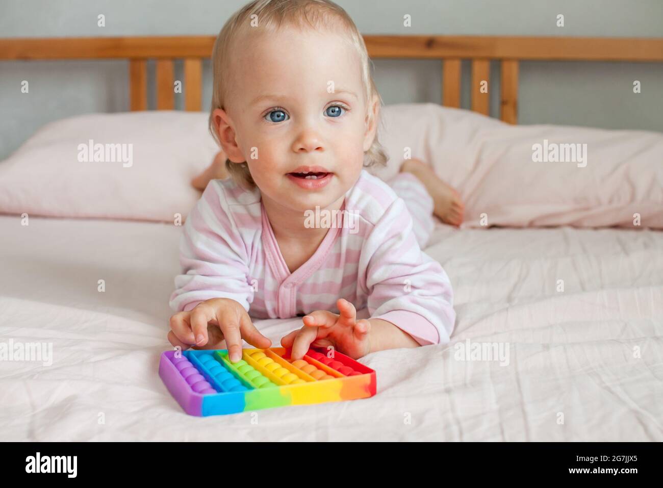 Little girl plays with trendy sensory toy pop it. The girl presses on colorful rainbow soft silicone bubbles. Relief of stress and anxiety. Stock Photo