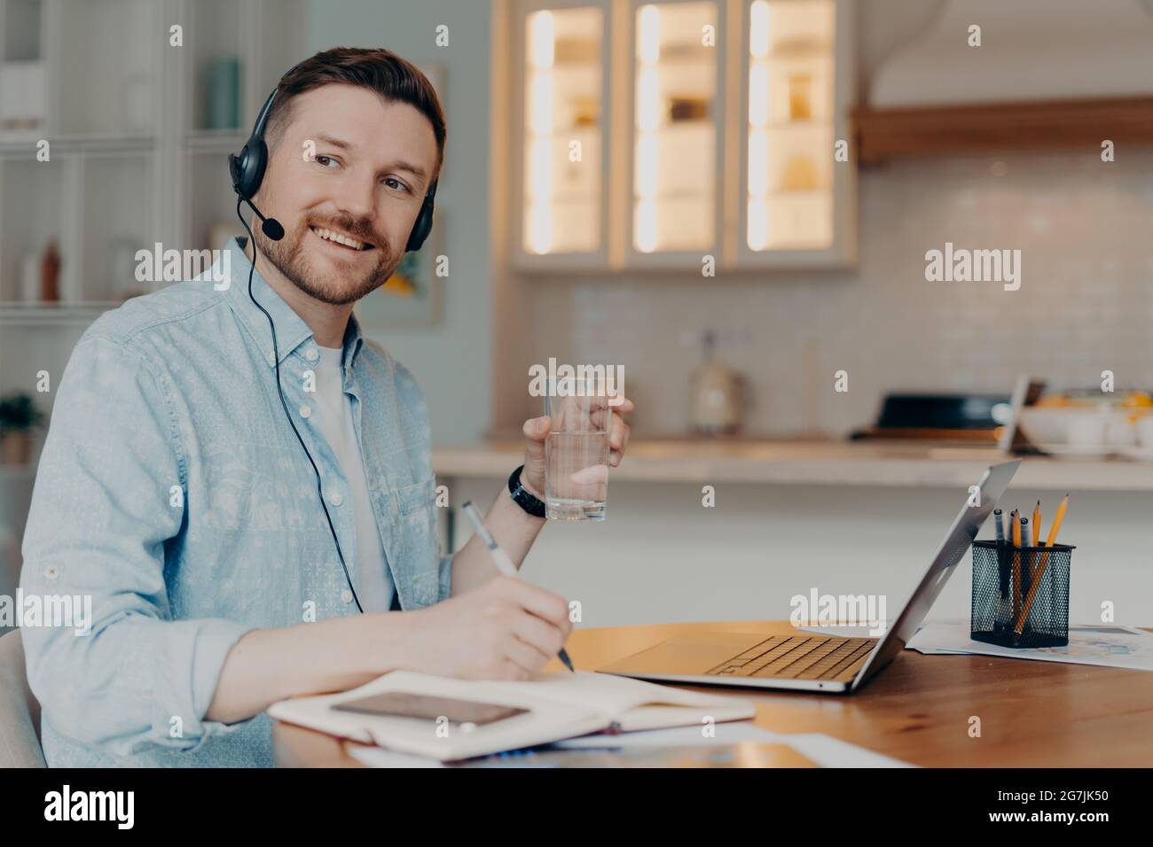 Bearded freelancer making notes in notebook while sitting at his workplace at home Stock Photo