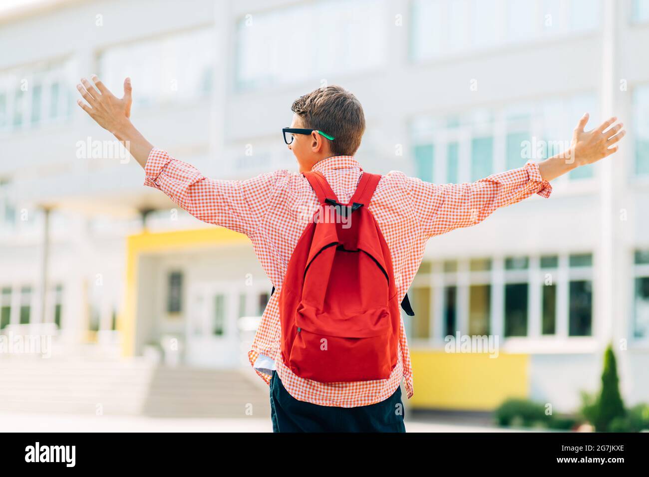 Rear view of a happy schoolboy boy, in glasses with a backpack, runs to school with pleasure, schoolboy boy on the background of the school, Back to s Stock Photo